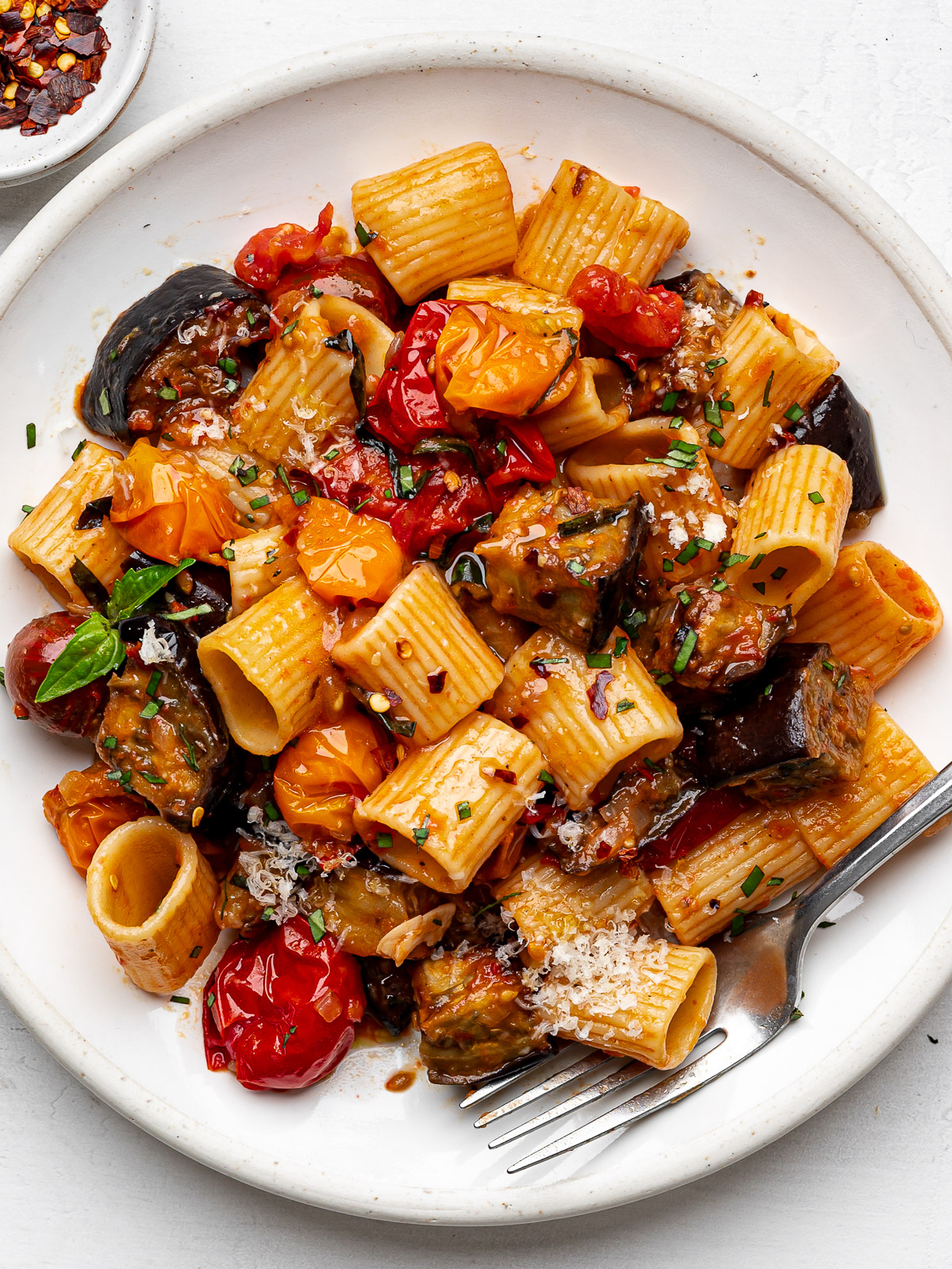 Roasted eggplant pasta served on a white plate garnished with fresh basil.