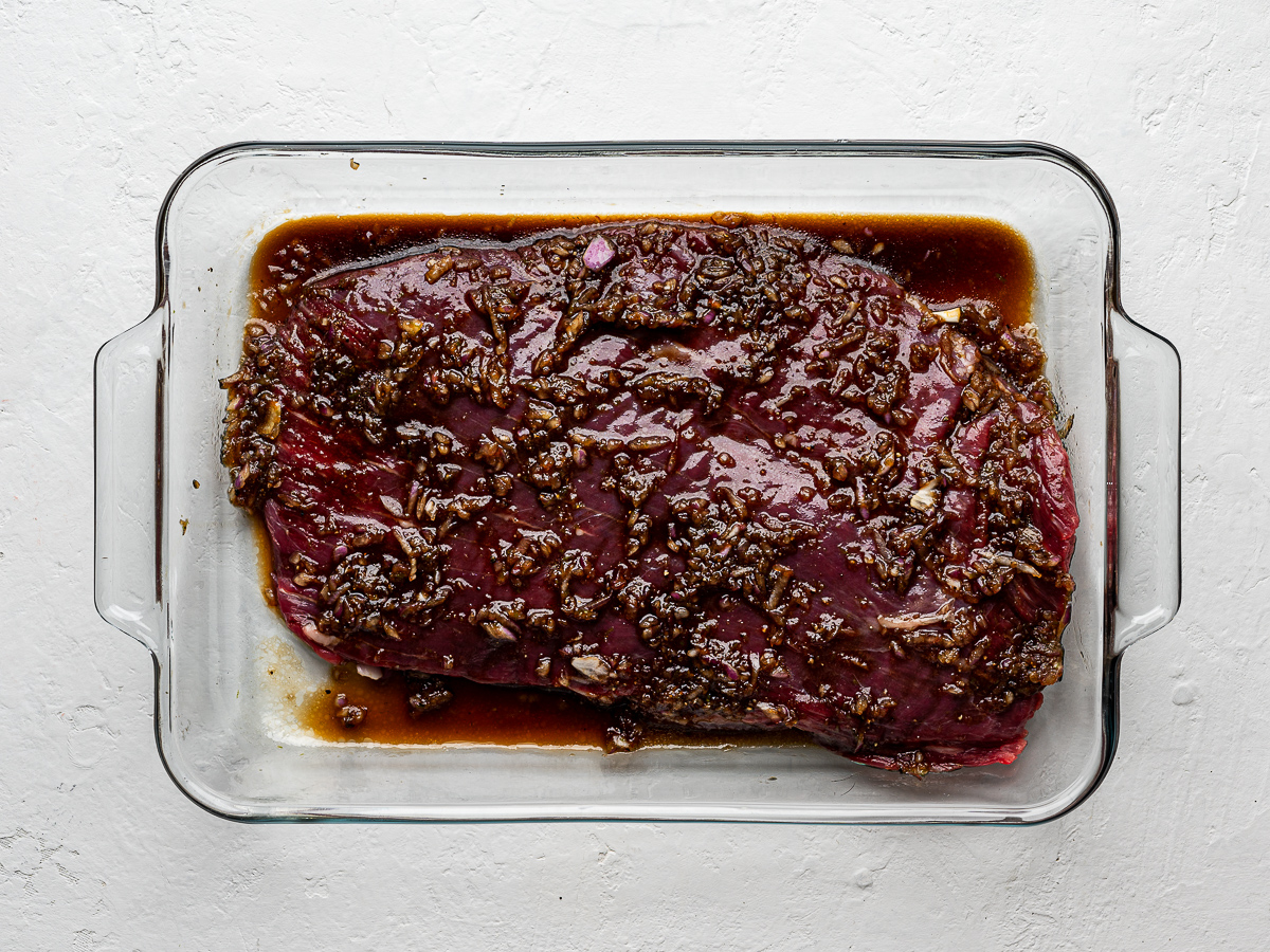 A whole piece of flank steak marinating in a glass dish.