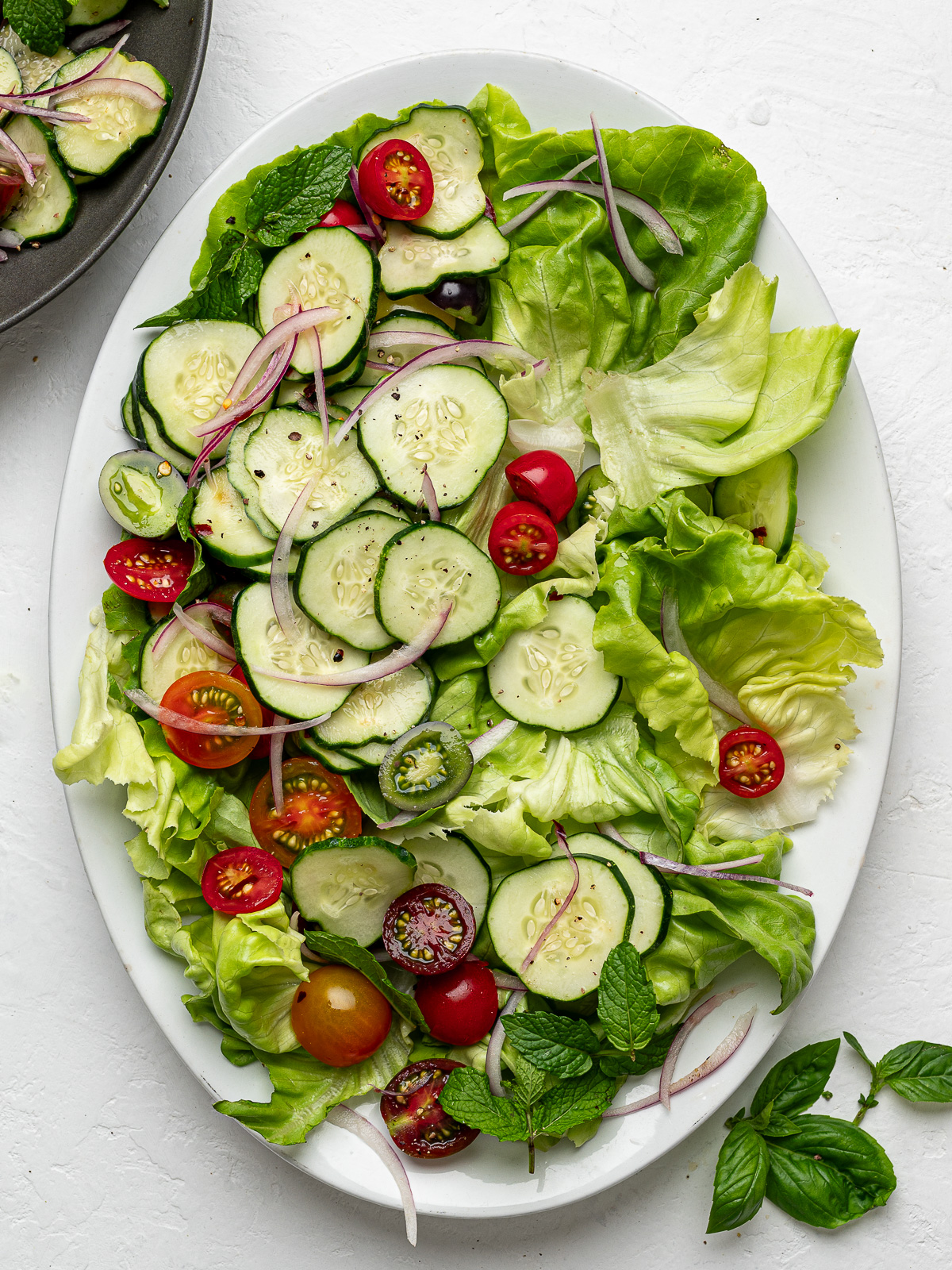 Lettuce placed in a single layer on a white platter topped with cucumbers and cherry tomatoes. 