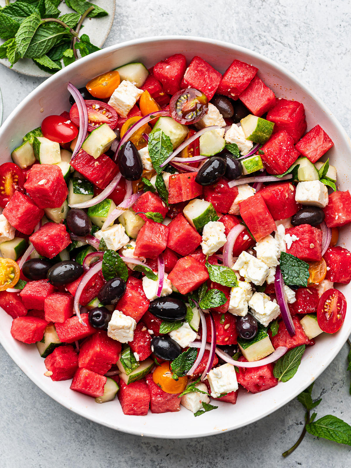 Watermelon salad served in white shallow bowl with bowl of fresh mint  on the side.