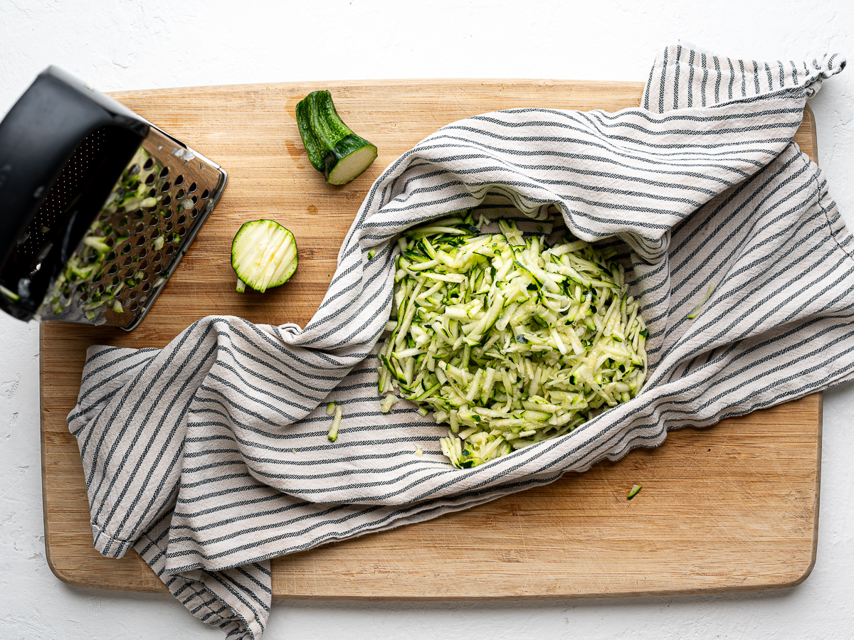 Grating zucchini with a box grater over a tea towel.