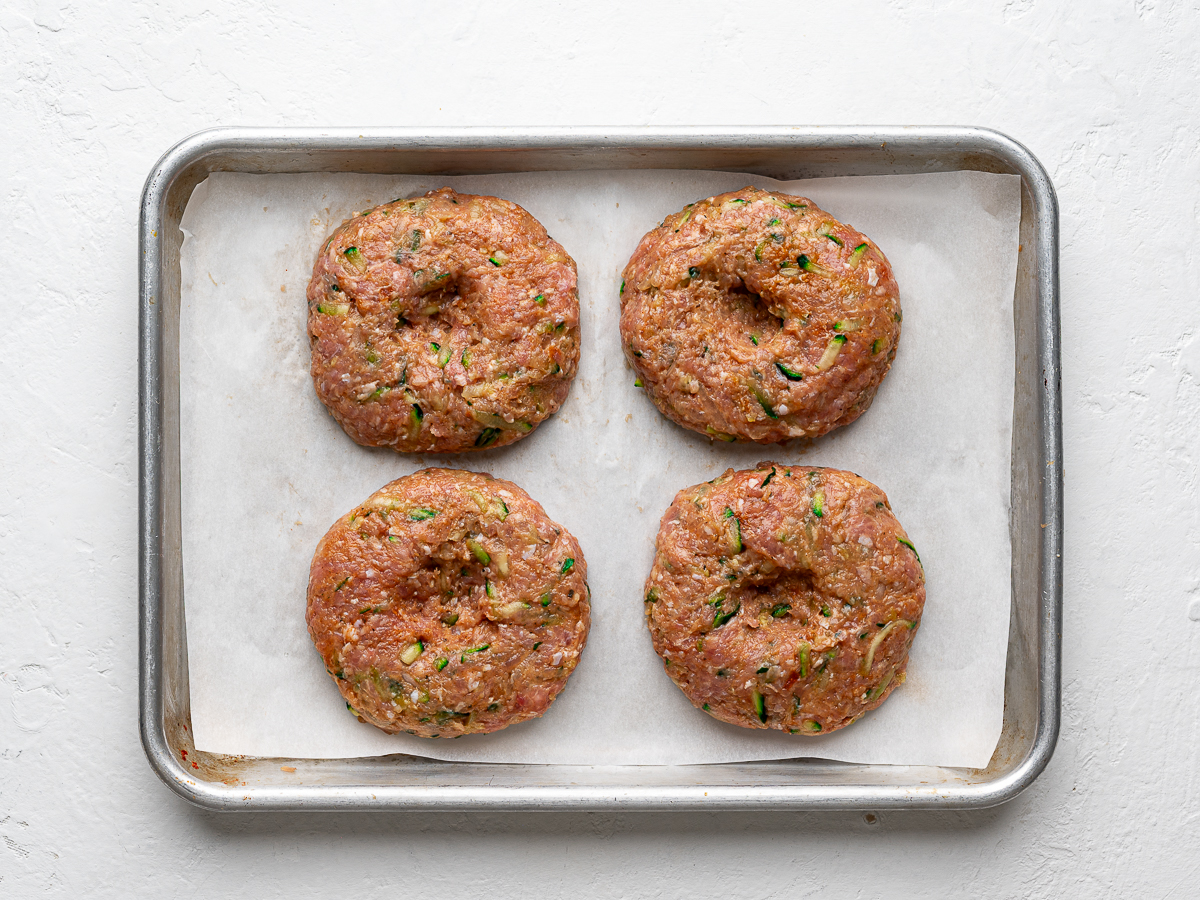 Four raw turkey patties on a small sheet pan.