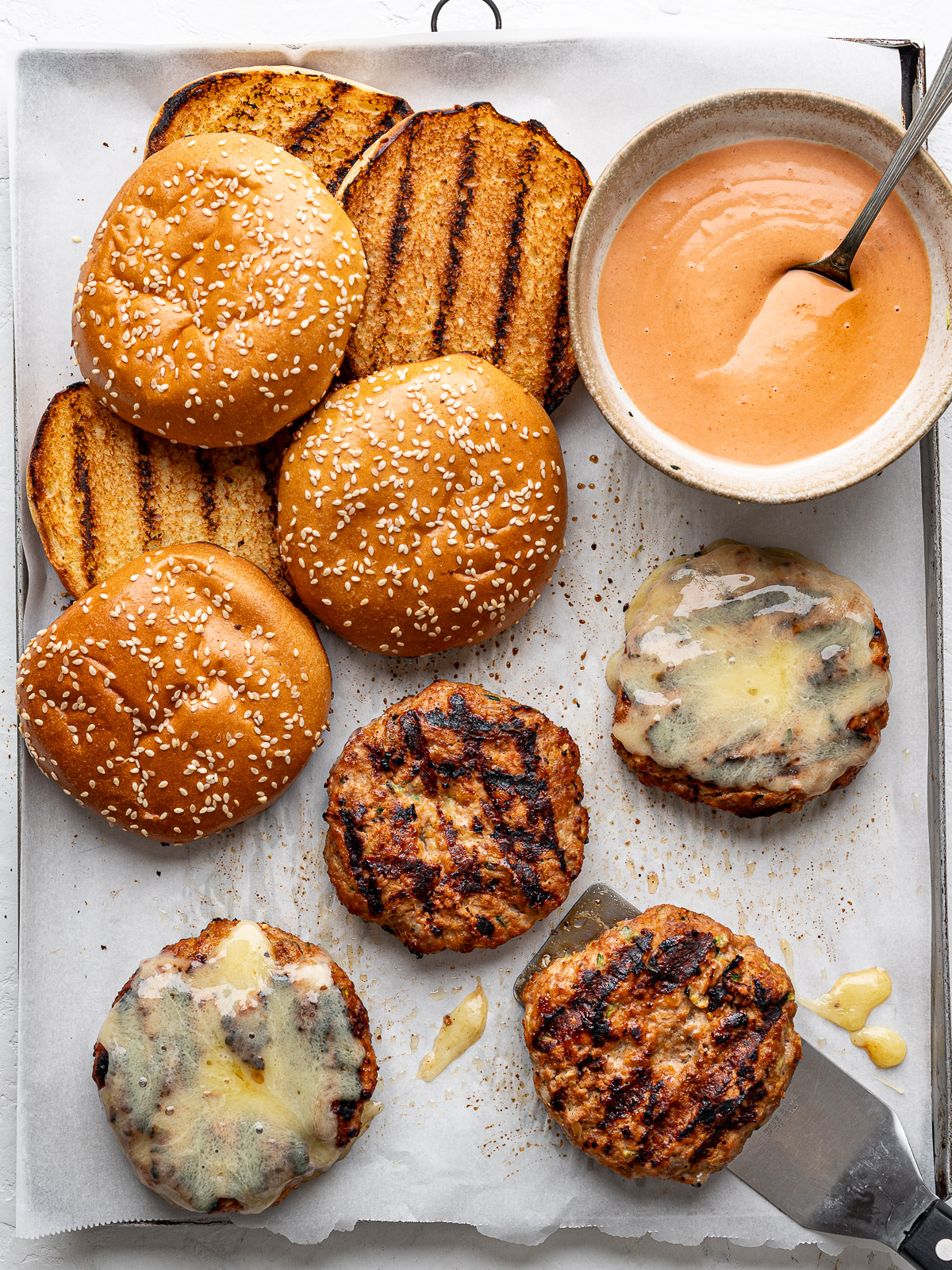 Cooked burger patties with buns and burger sauce on the side. 