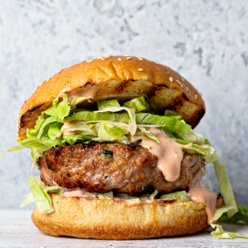 Side-view of a hamburger bun filled with a Turkey zucchini burger, iceberg lettuce and burger sauce.