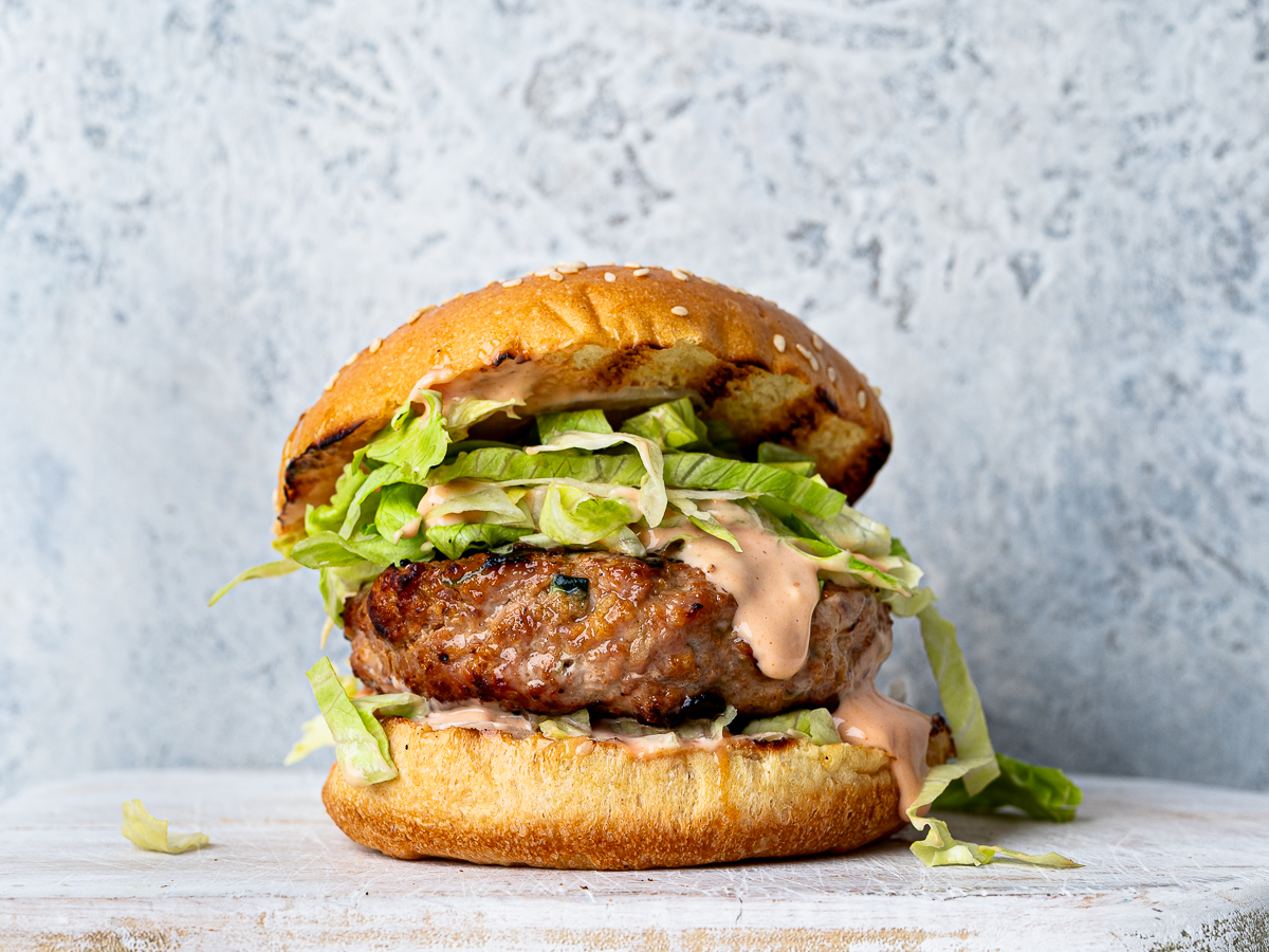 Side-view of a hamburger bun filled with a Turkey zucchini burger, iceberg lettuce and burger sauce.