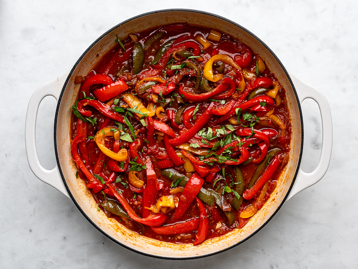 Fresh chopped basil added to cooked peperonata in pan.