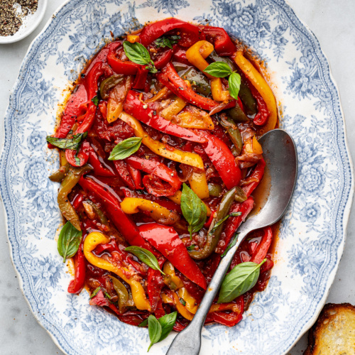Peperonata (stewed peppers) served on a platter with a serving spoon and crusty bread on the side.