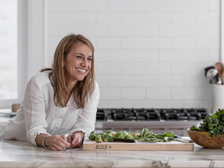 Sandra Valvassori leaning over her kitchen counter smiling while she prepared food.