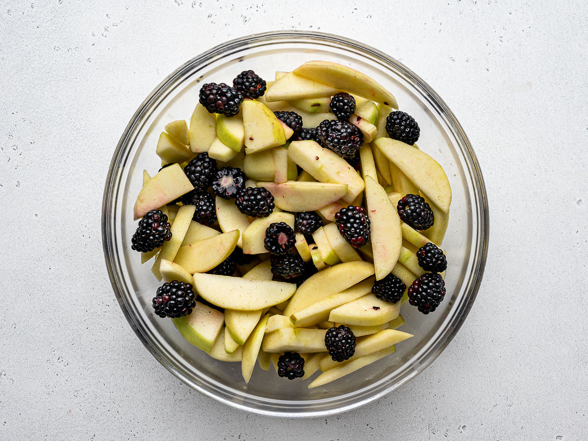 sliced apples with blackberries added in glass mixing bowl.