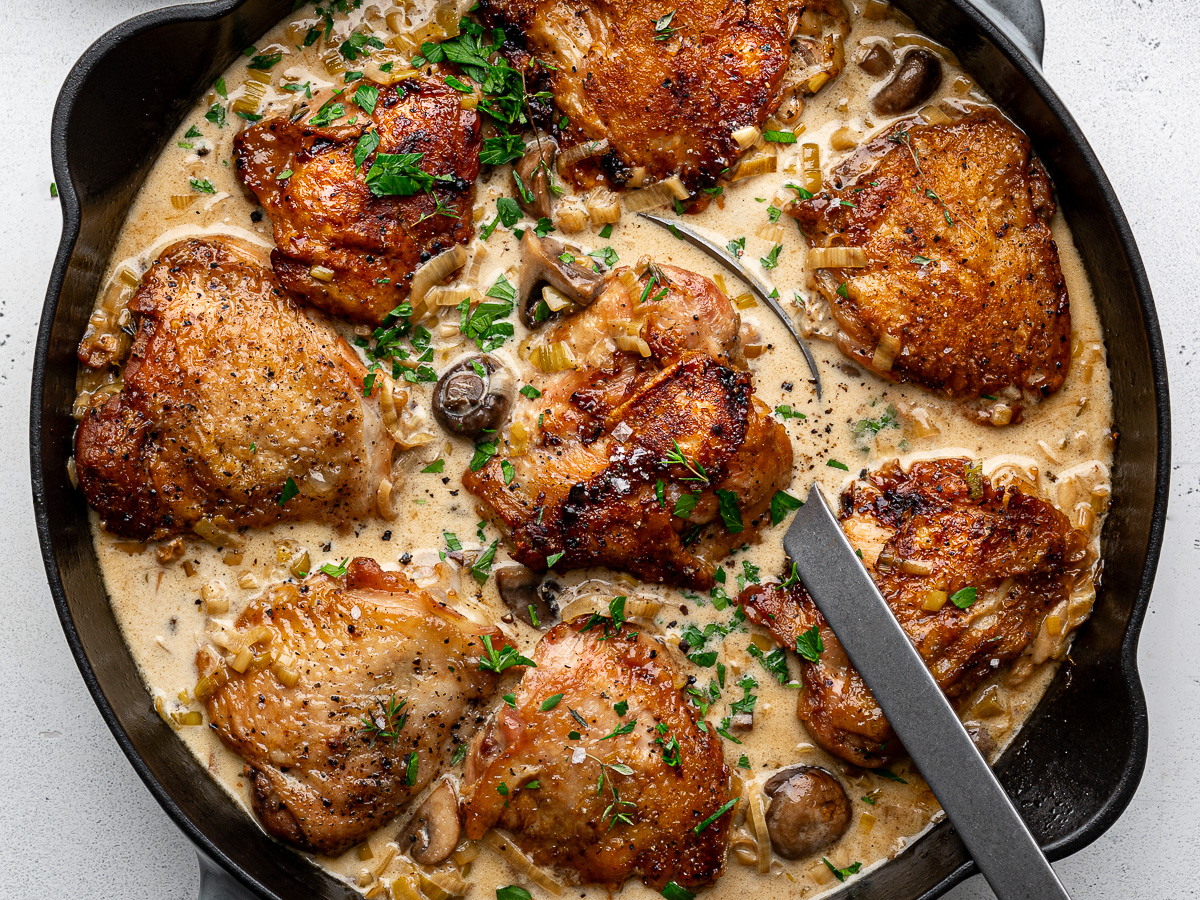 Close up of the finished dish of creamy chicken and leeks in the skillet with a large serving spoon.