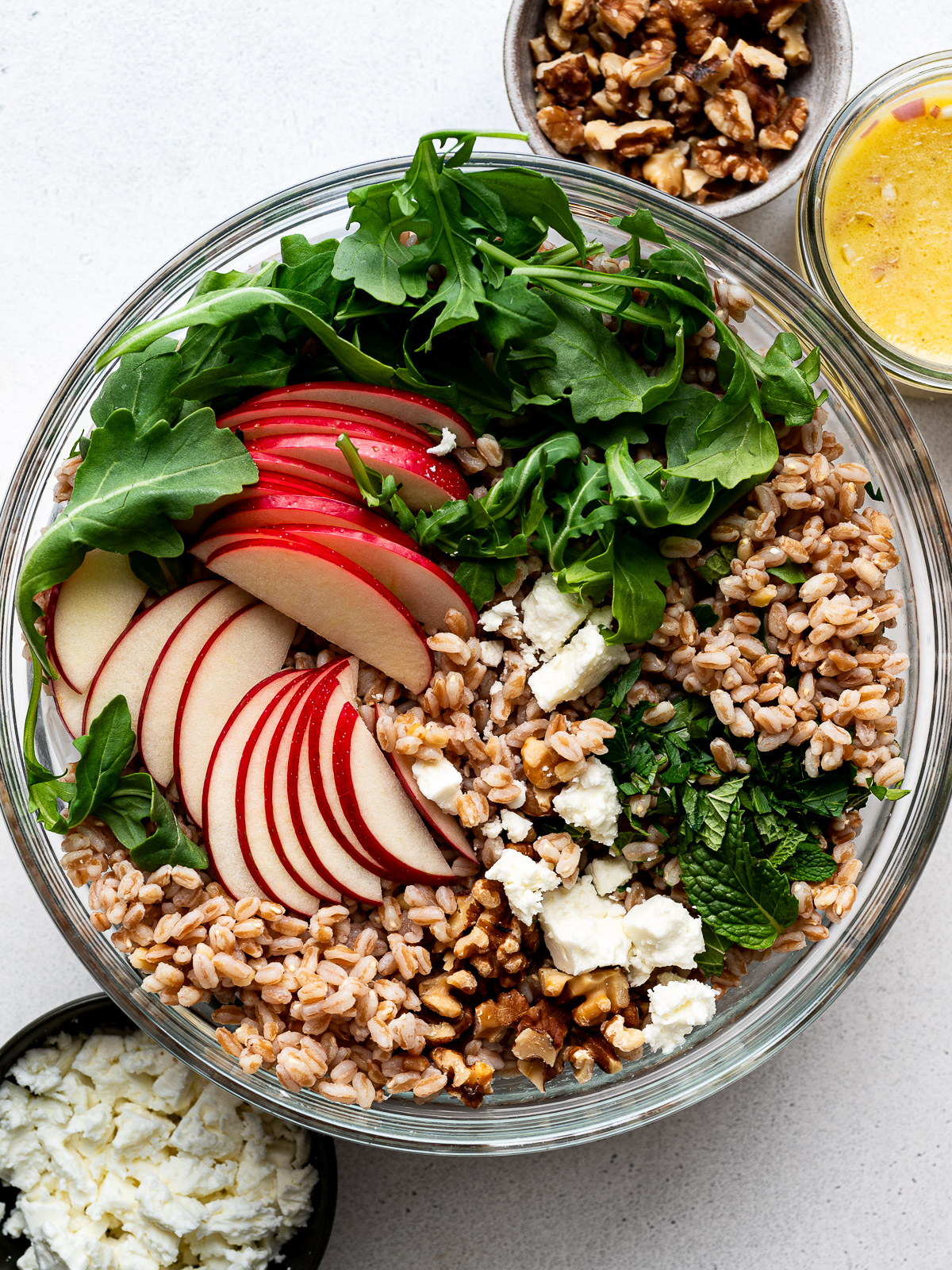 Sliced apples, arugula, feta, herbs and walnuts added to the bowl with farro.