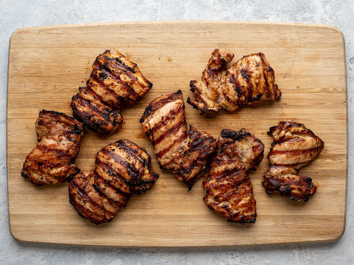 Grilled chicken thighs on a cutting board.