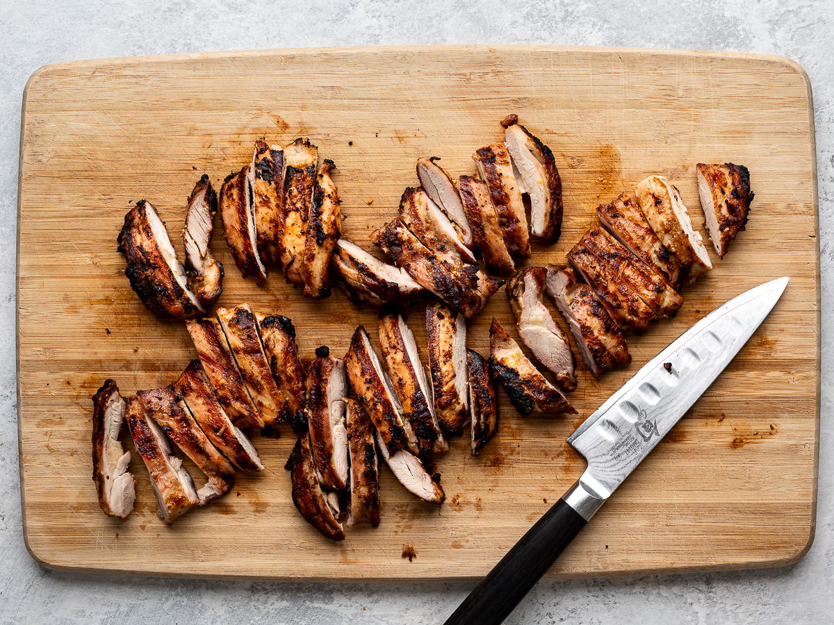 Slices of grilled chicken thighs on a cutting board. 
