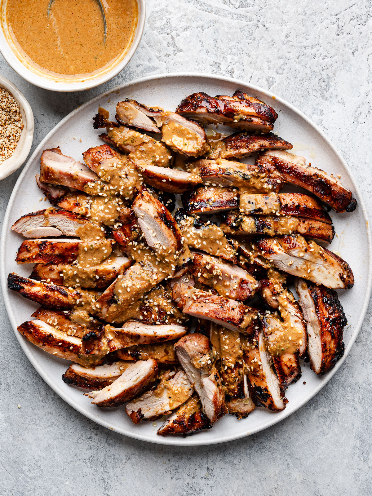 Slices of grilled chicken on a round white platter drizzled with sesame ginger dressing.