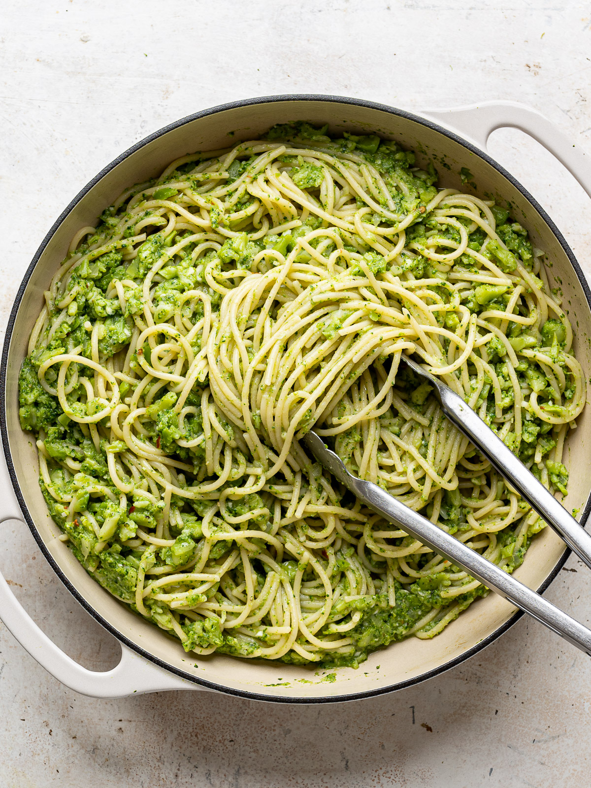 Tossing pasta with smashed broccoli in skillet.