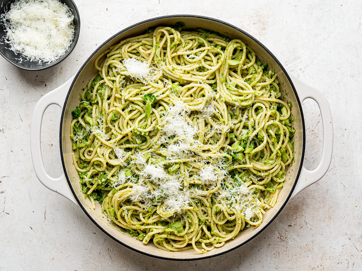 Adding grated cheese to broccoli pasta in skillet.