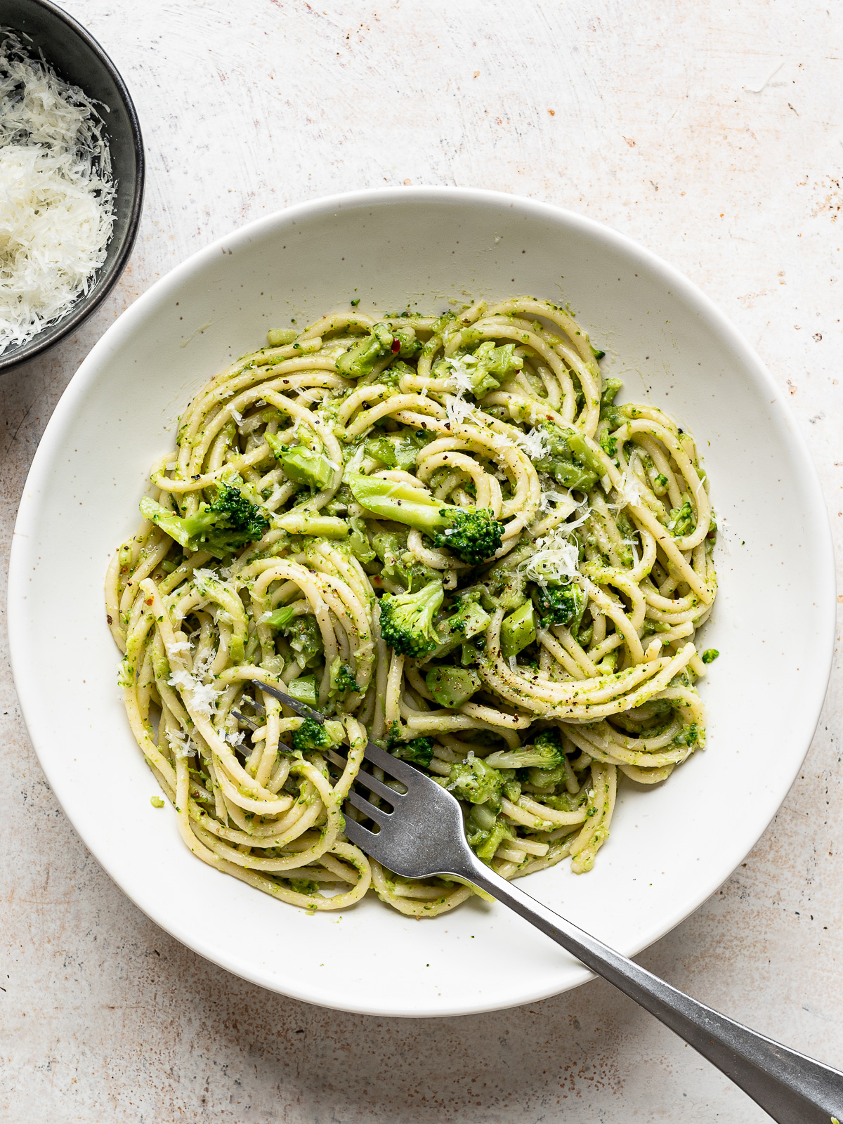 Broccoli Pasta served in white bowl with grated pecorino on the side.