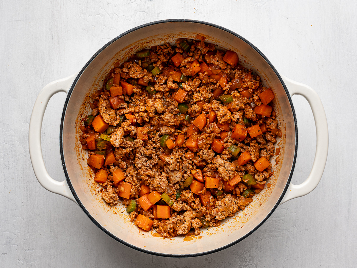Browned ground turkey with vegetables in white pot. 