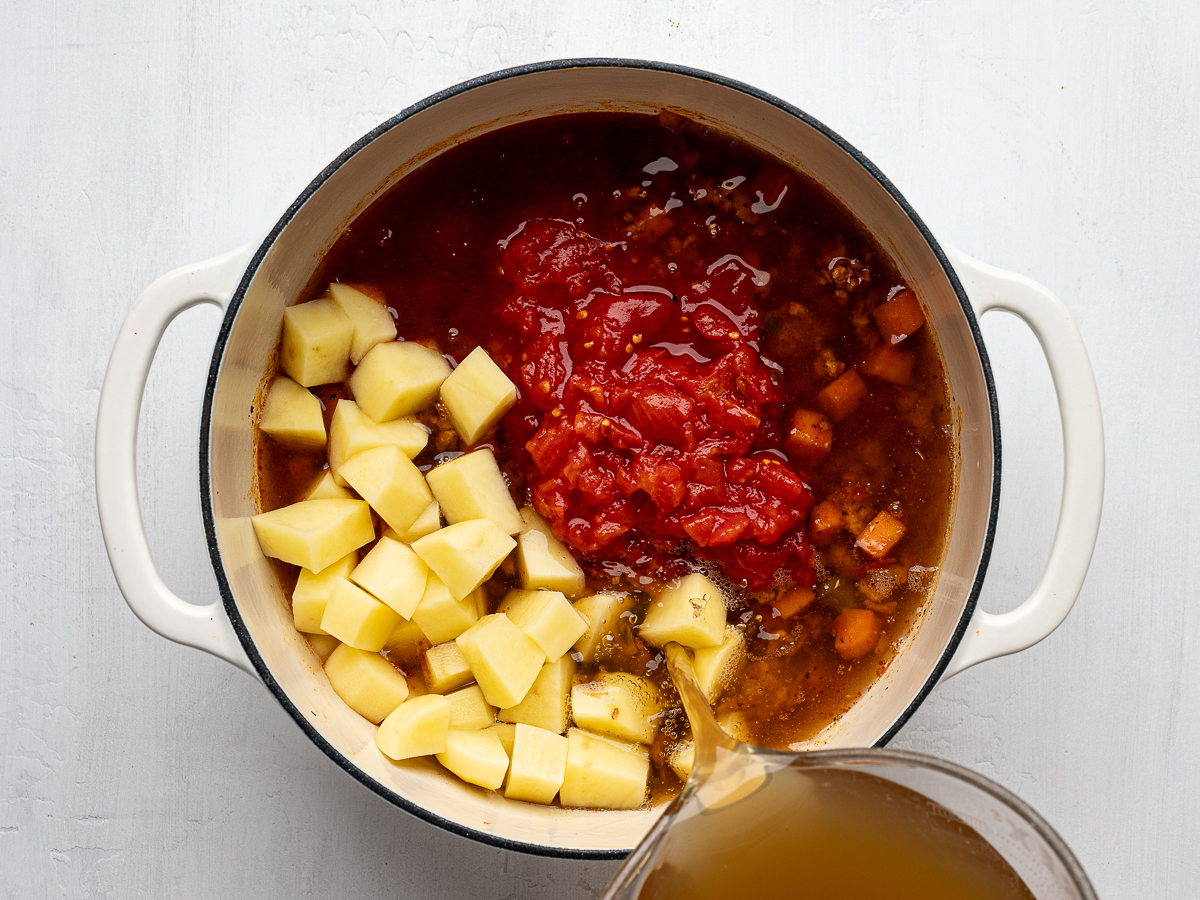 Chopped potatoes, crushed tomatoes and broth, added to the pot. 