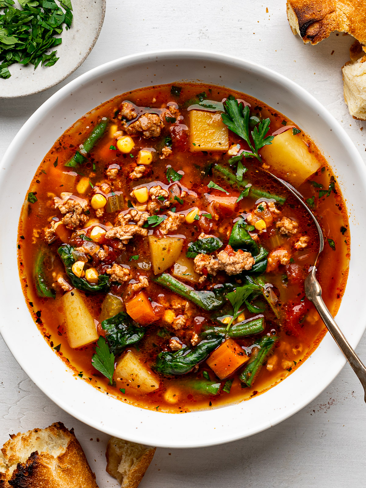 Ground turkey soup with vegetables served in a white bowl with crusty bread on the side.