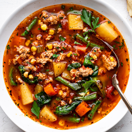 Ground turkey soup with vegetables served in a white bowl with crusty bread on the side.