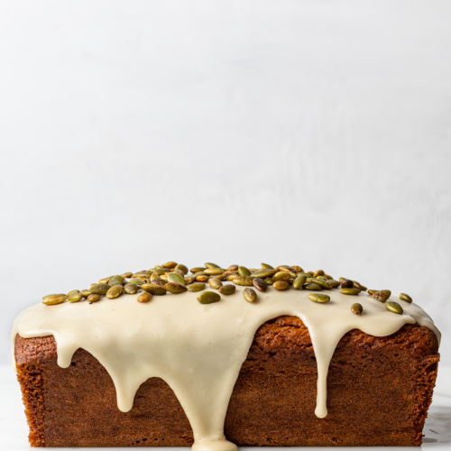 Side view of gluten-free pumpkin loaf drizzled with glaze and topped with pepitas.