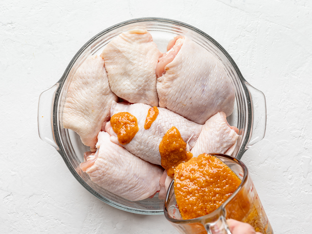 Pouring miso marinade over chicken thighs in glass bowl. 