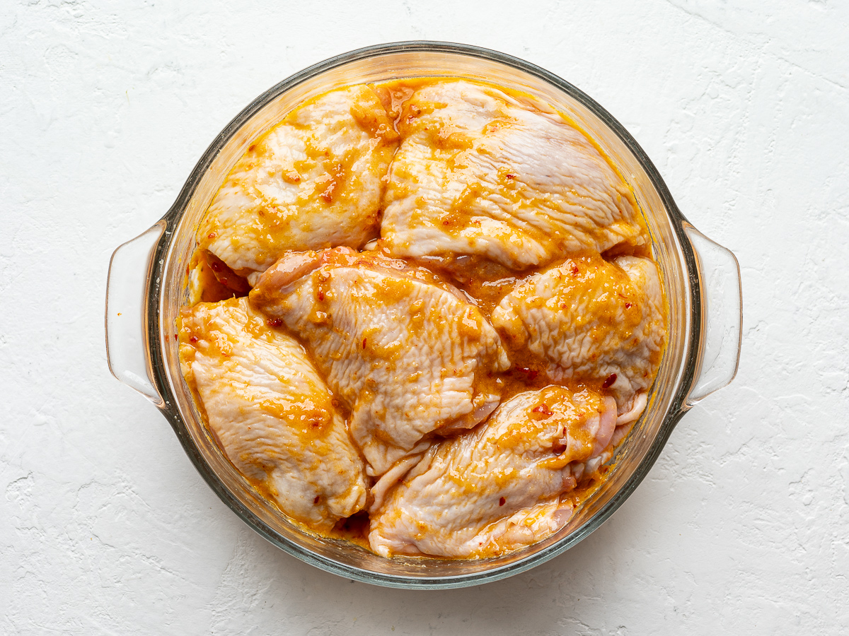 Chicken thighs marinating in glass bowl.