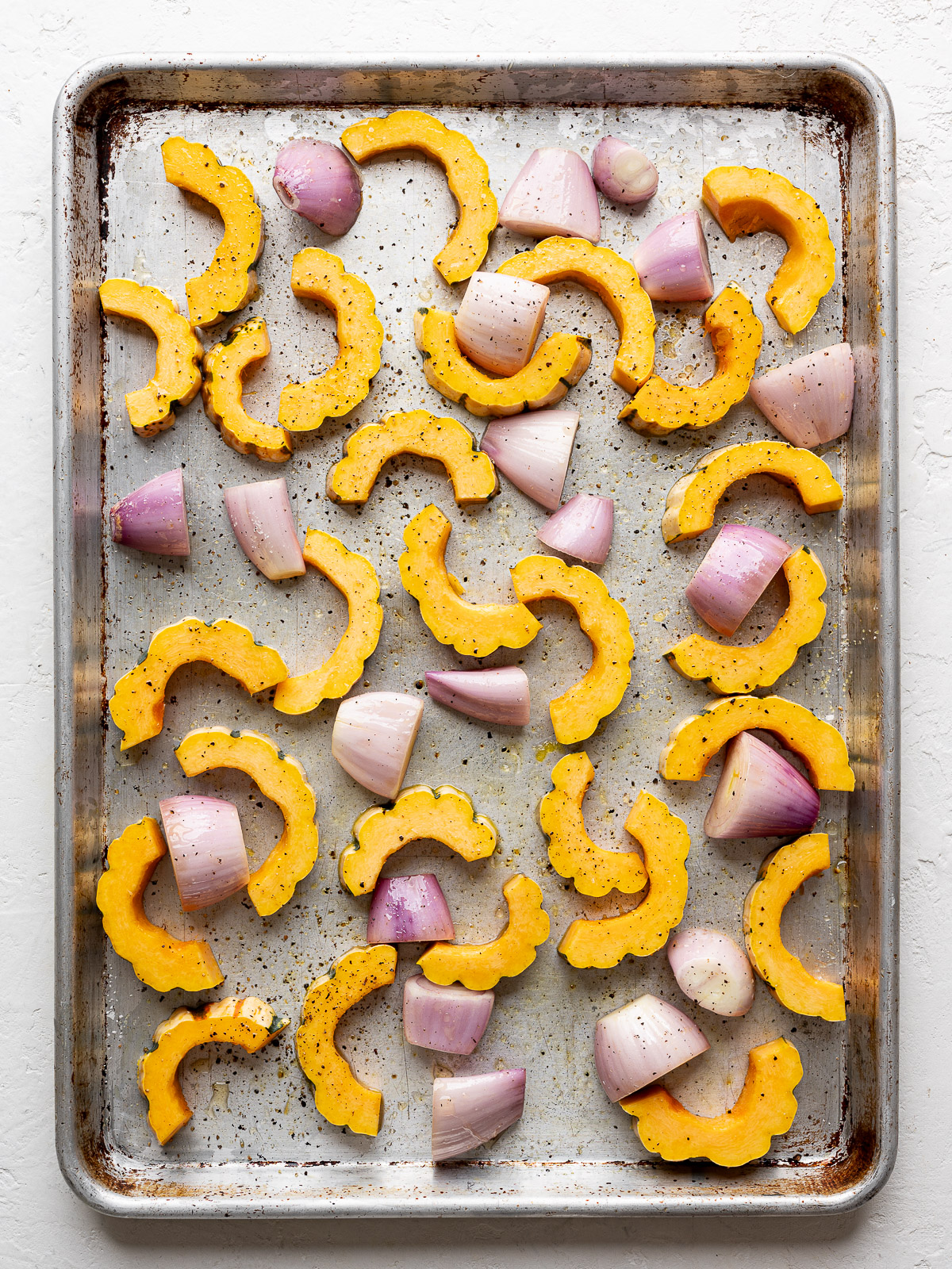 Half-moon delicata squash slices on sheet pan with shallots. 