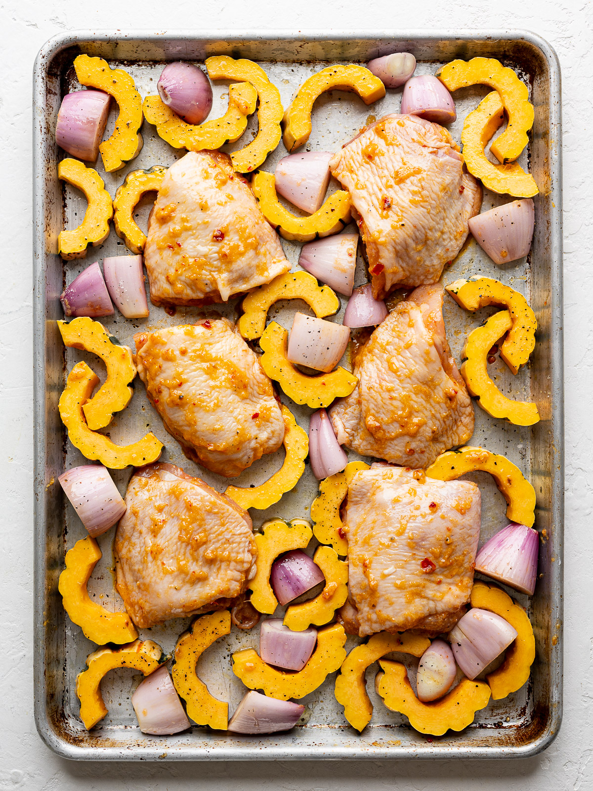 Raw chicken thighs nestled in-between uncooked vegetables on sheet pan. 
