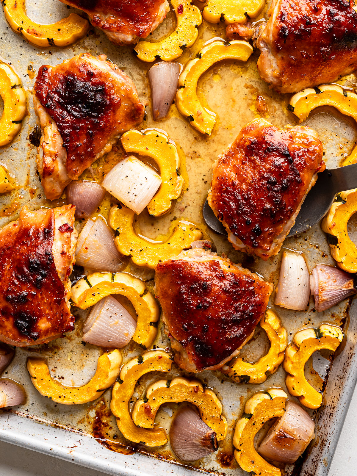 Large serving spoon scooping out one chicken piece from sheet pan. 
