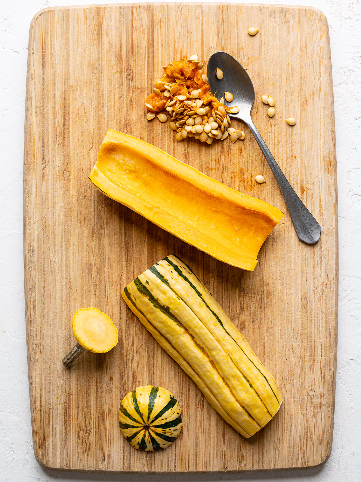 Delicata squash cut in half lengthwise on a cutting board with seeds scooped out of one half.