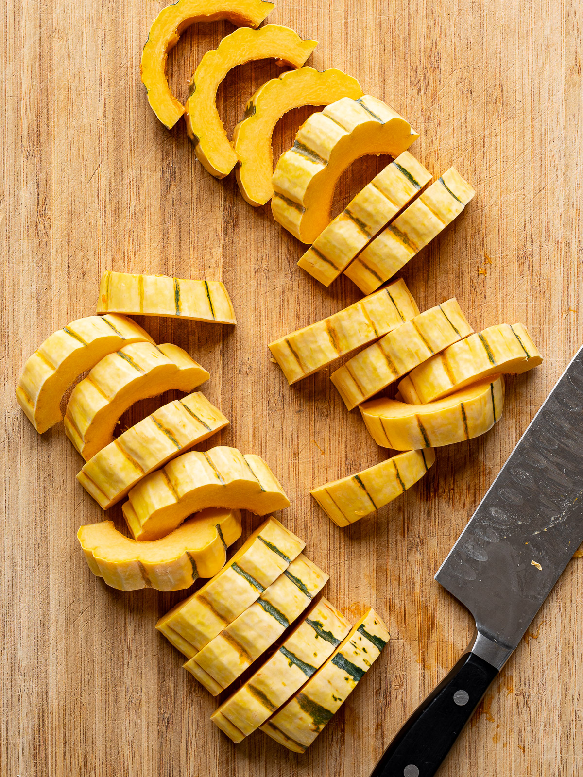 Delicata squash cut into half-moon slices on a cutting board.  