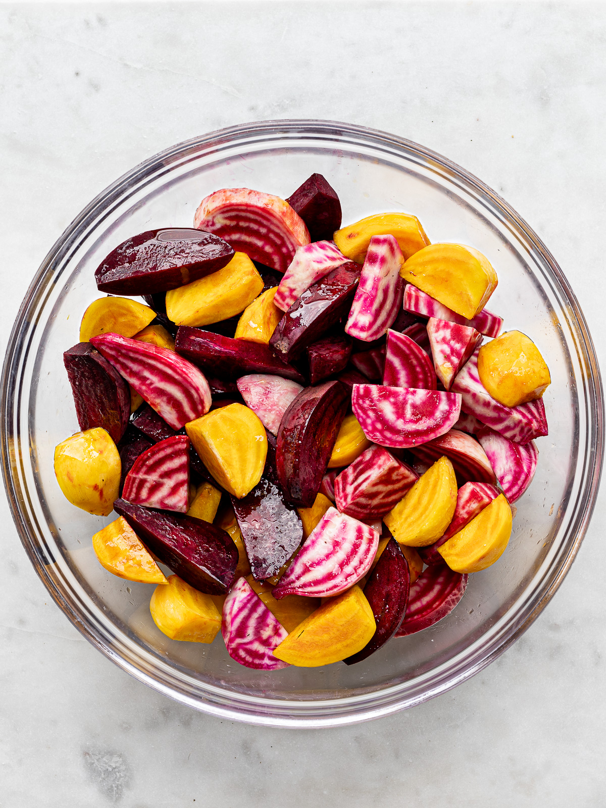 Sliced beets in mixing bowl tossed with olive oil and seasonings.