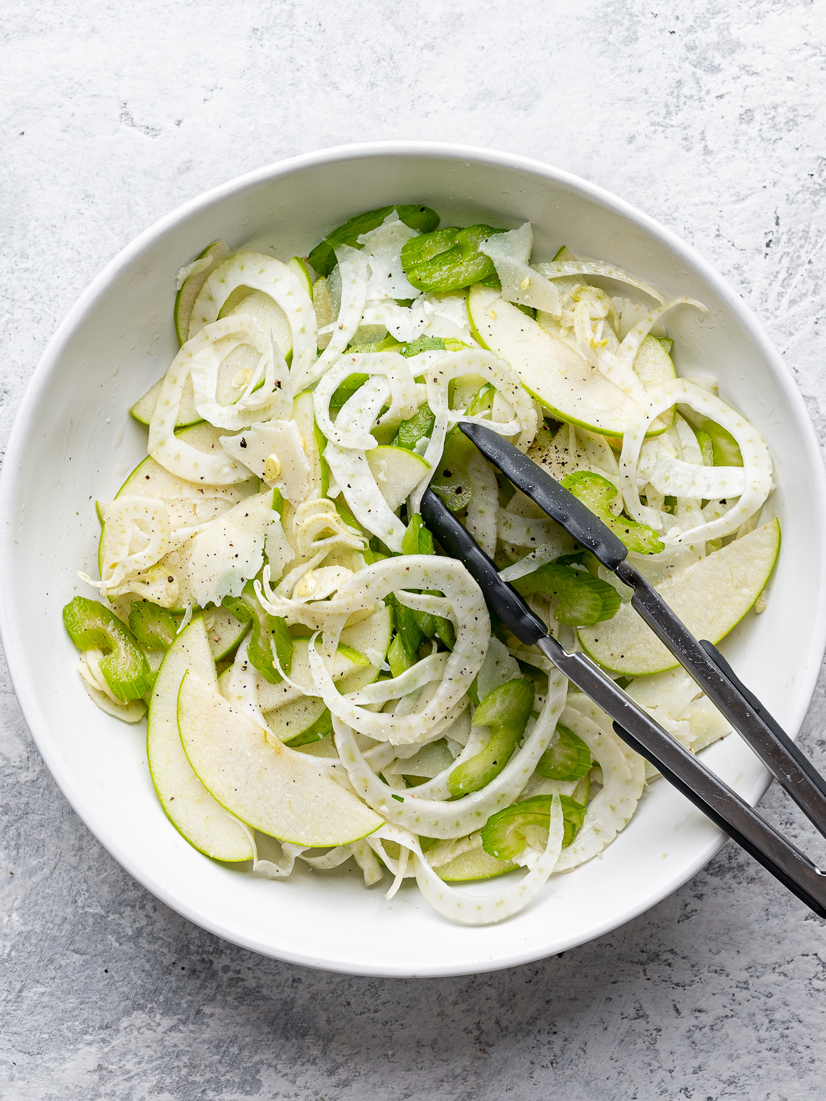 Salad tossed in white bowl with dressing. 