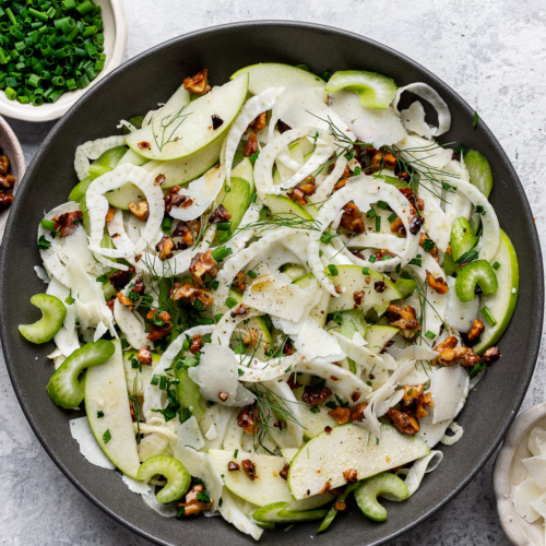 Assembled apple fennel salad served on a gray serving bowl topped with walnuts and manchego cheese.