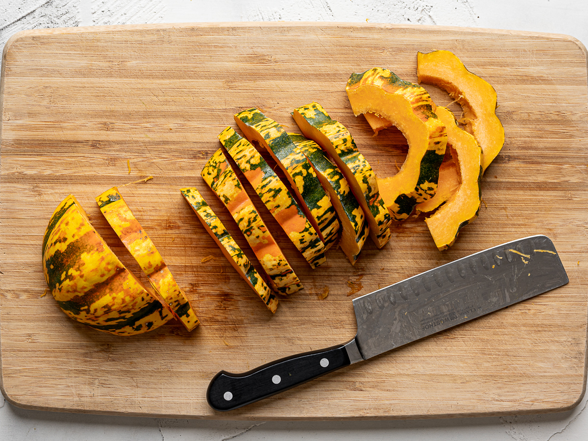 Carnival squash sliced into half-moon slices on cutting board. 
