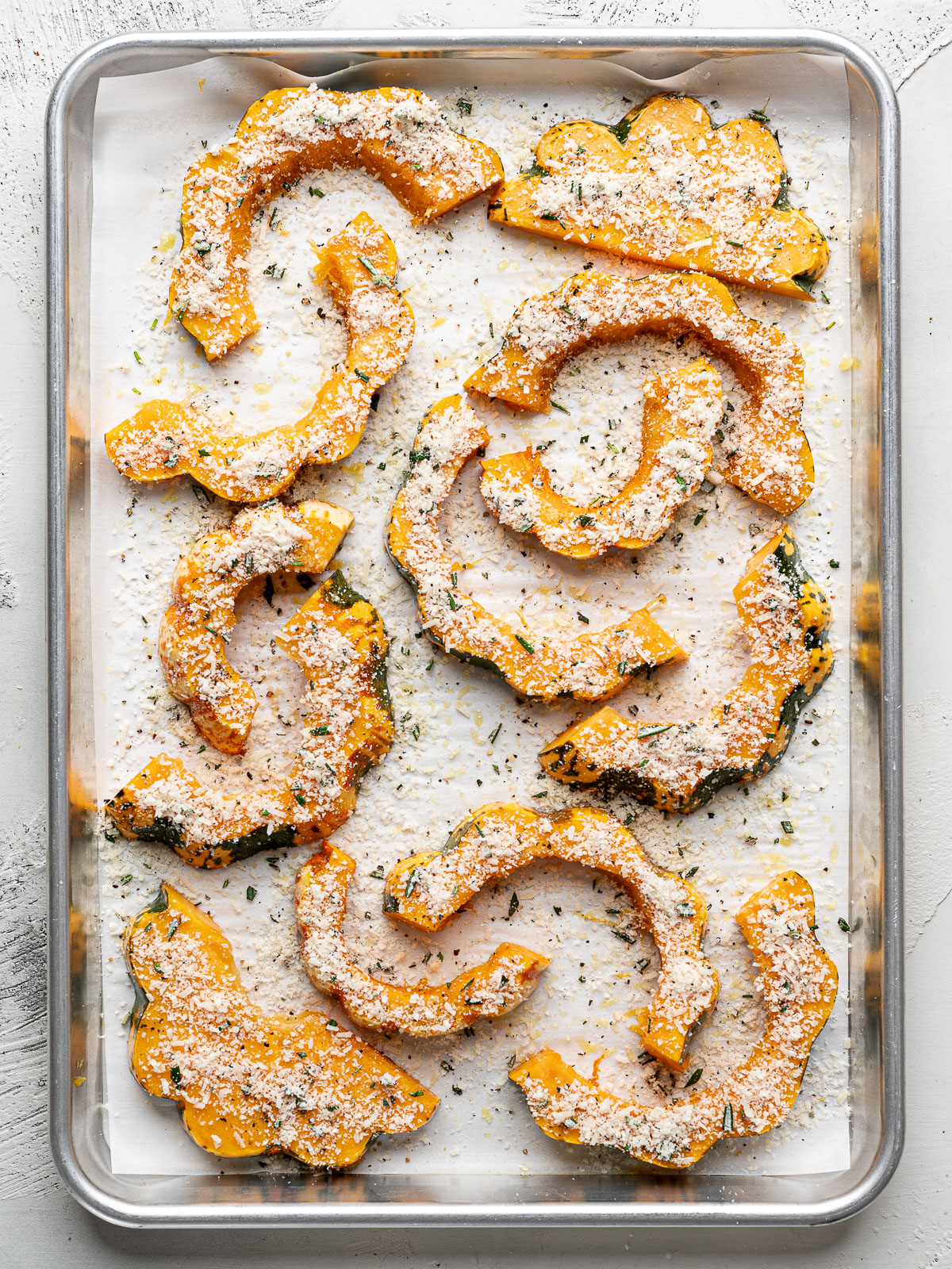 Squash slices on baking sheet sprinkled with parmesan cheese and chopped fresh rosemary.