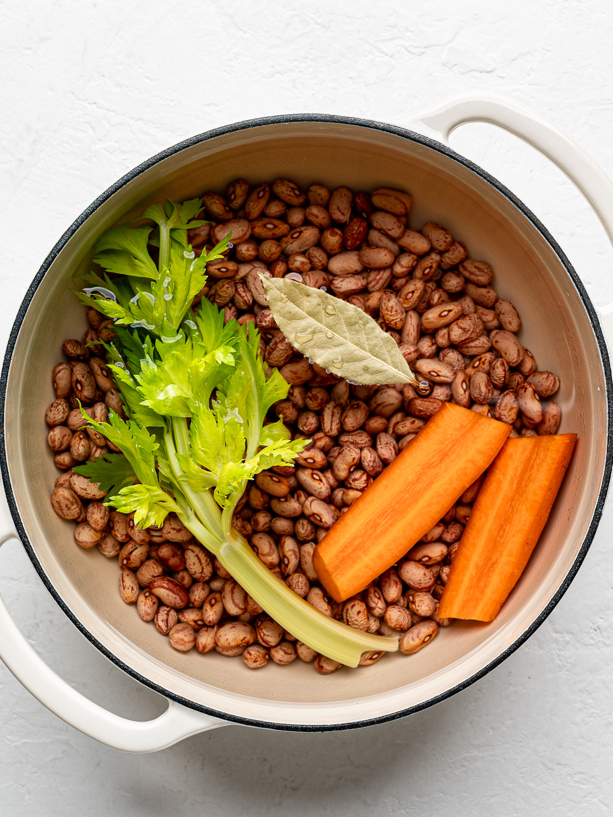 Dried beans in pot with water and aromatics.