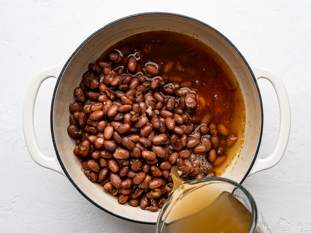 Pouring broth into pot with beans.
