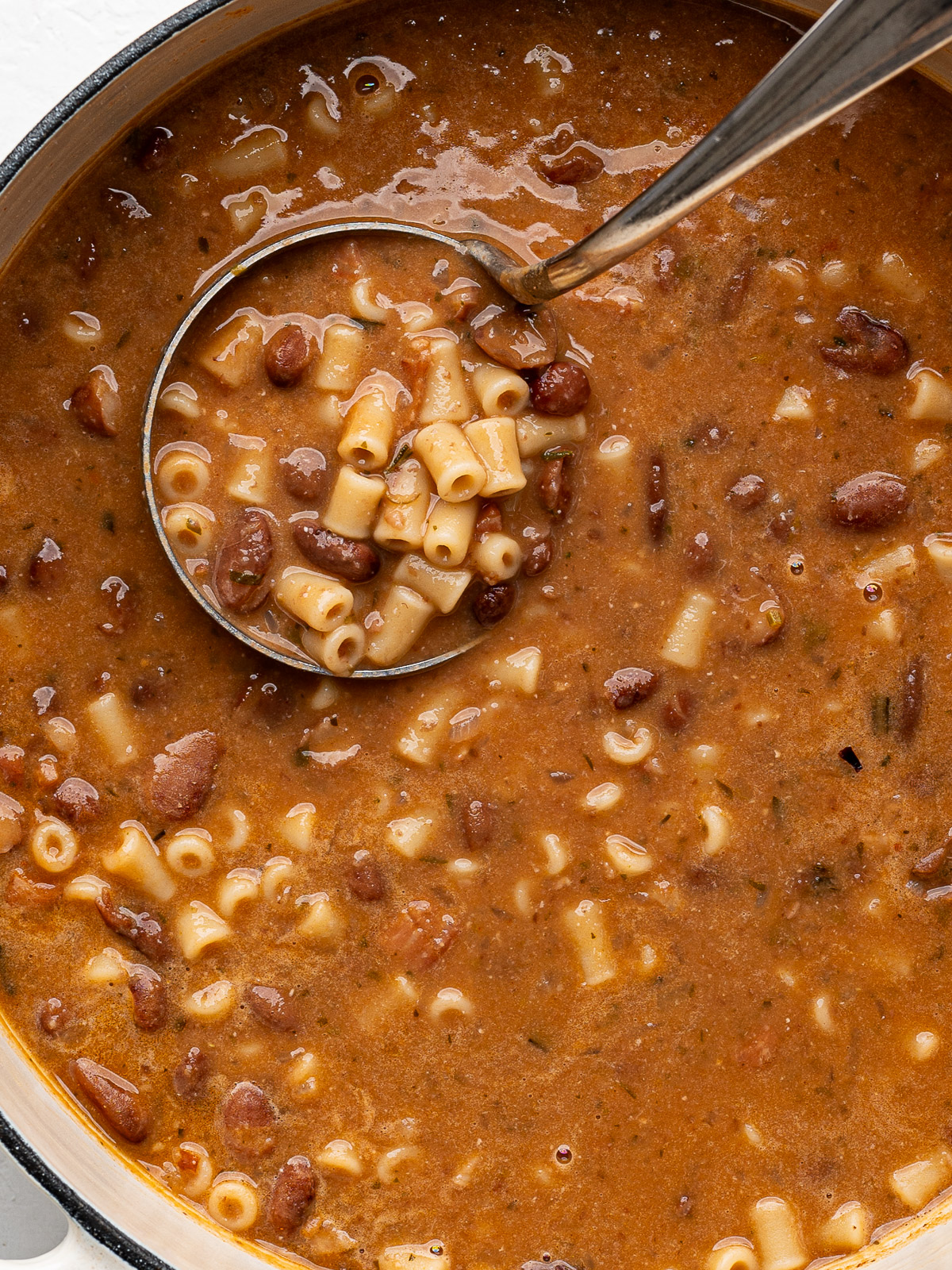 Close up of a ladle scooping up some pasta e fagioli from pot. 