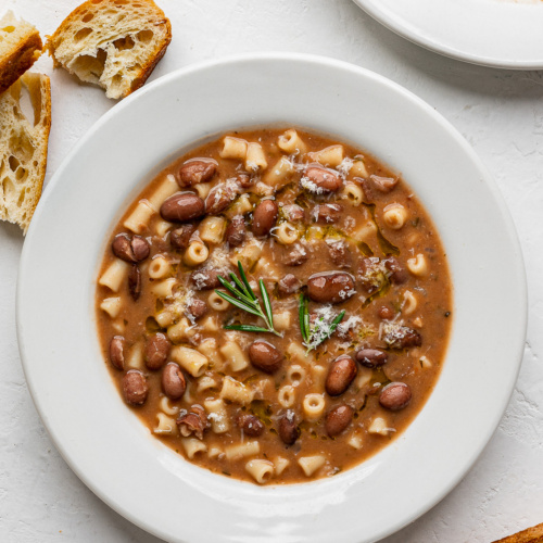 Pasta e fagioli served in two white bowls with crusty bread on the side.