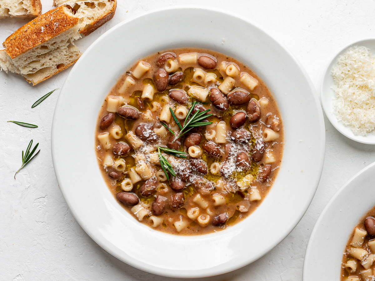 Pasta e fagioli served in two white bowls with cheese and crusty bread on the side.