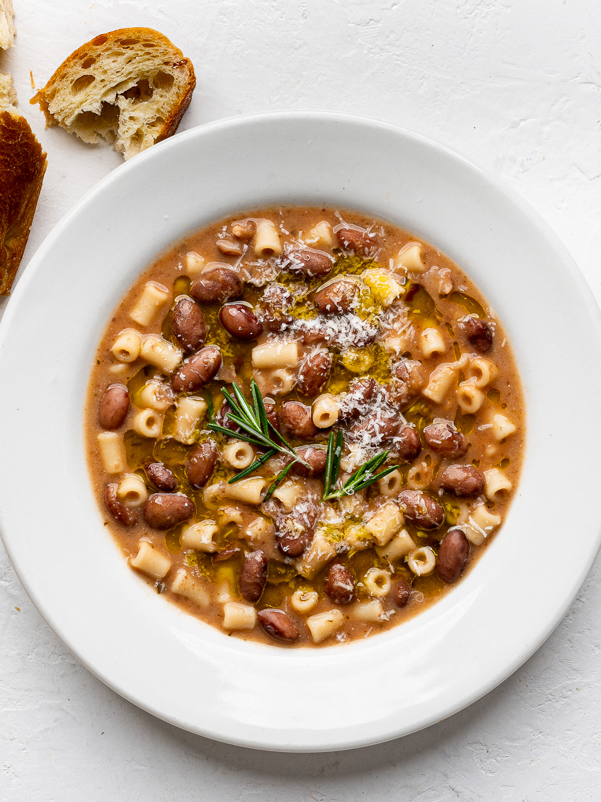 Bean and pasta soup served in a white bowl with crusty bread on the side. 