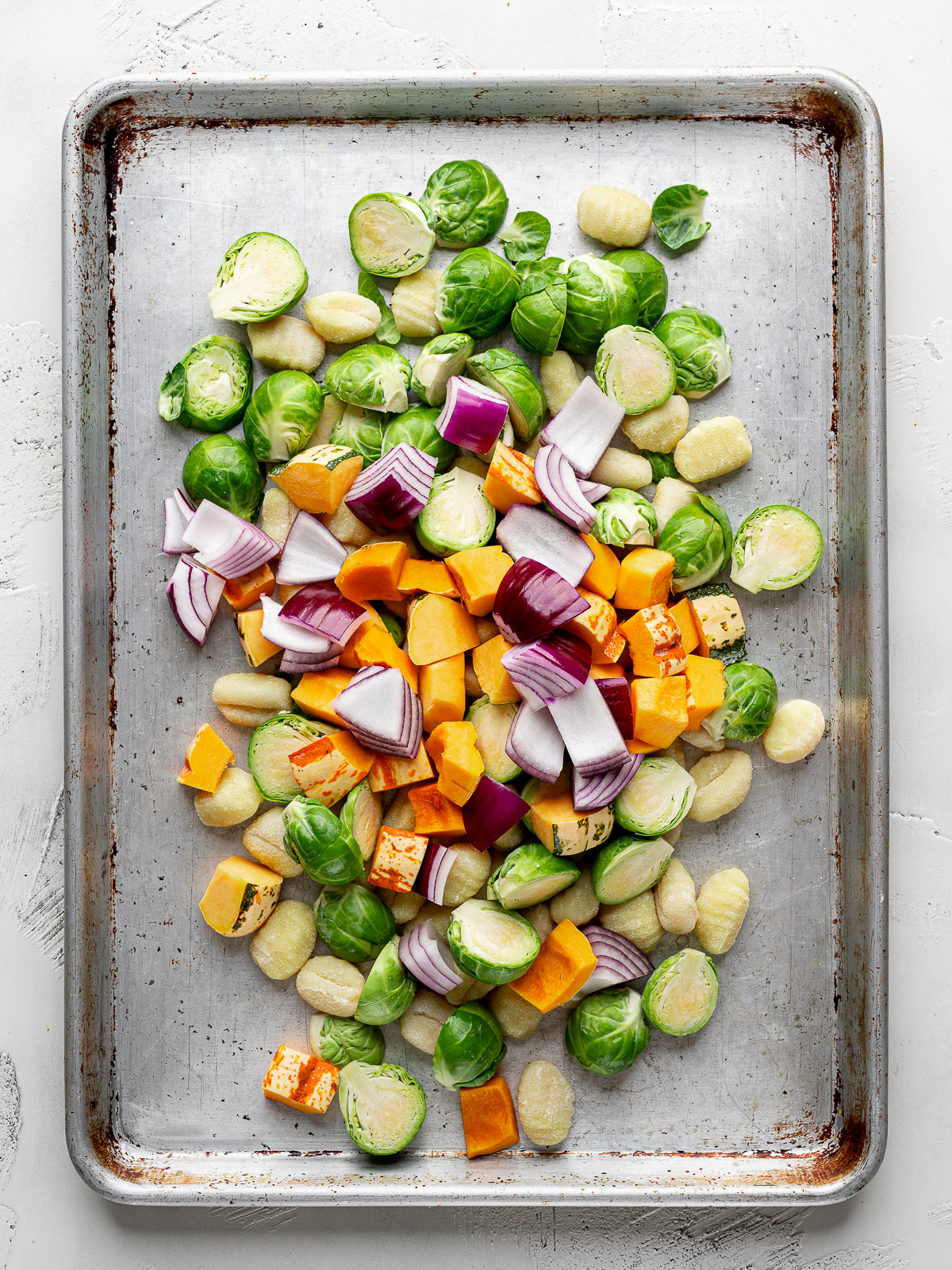 Uncooked gnocchi, Brussels sprouts, squash and red onion piled on a sheet 