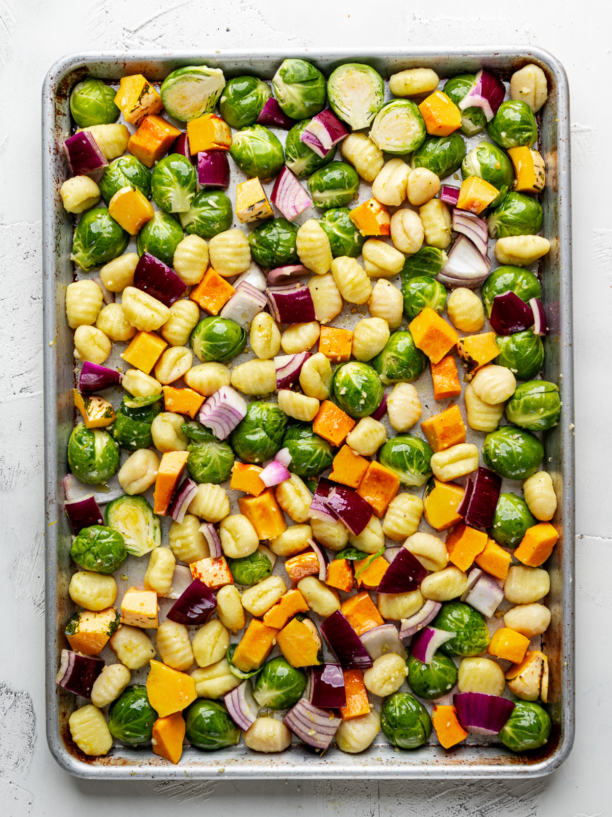 Uncooked gnocchi, Brussels sprouts, squash and red onion tossed with dressing and spread out on a sheet pan. 