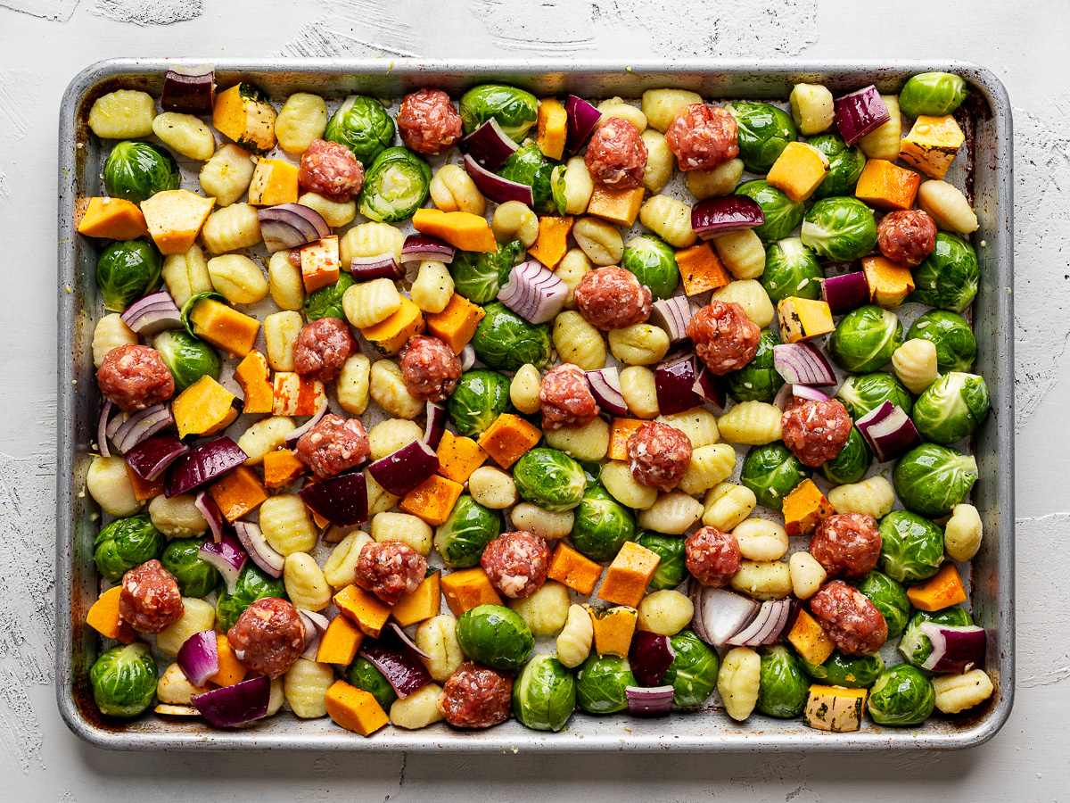 Uncooked gnocchi, sausage, Brussels sprouts, squash and red onion tossed with dressing and spread out evenly on a sheet pan. 