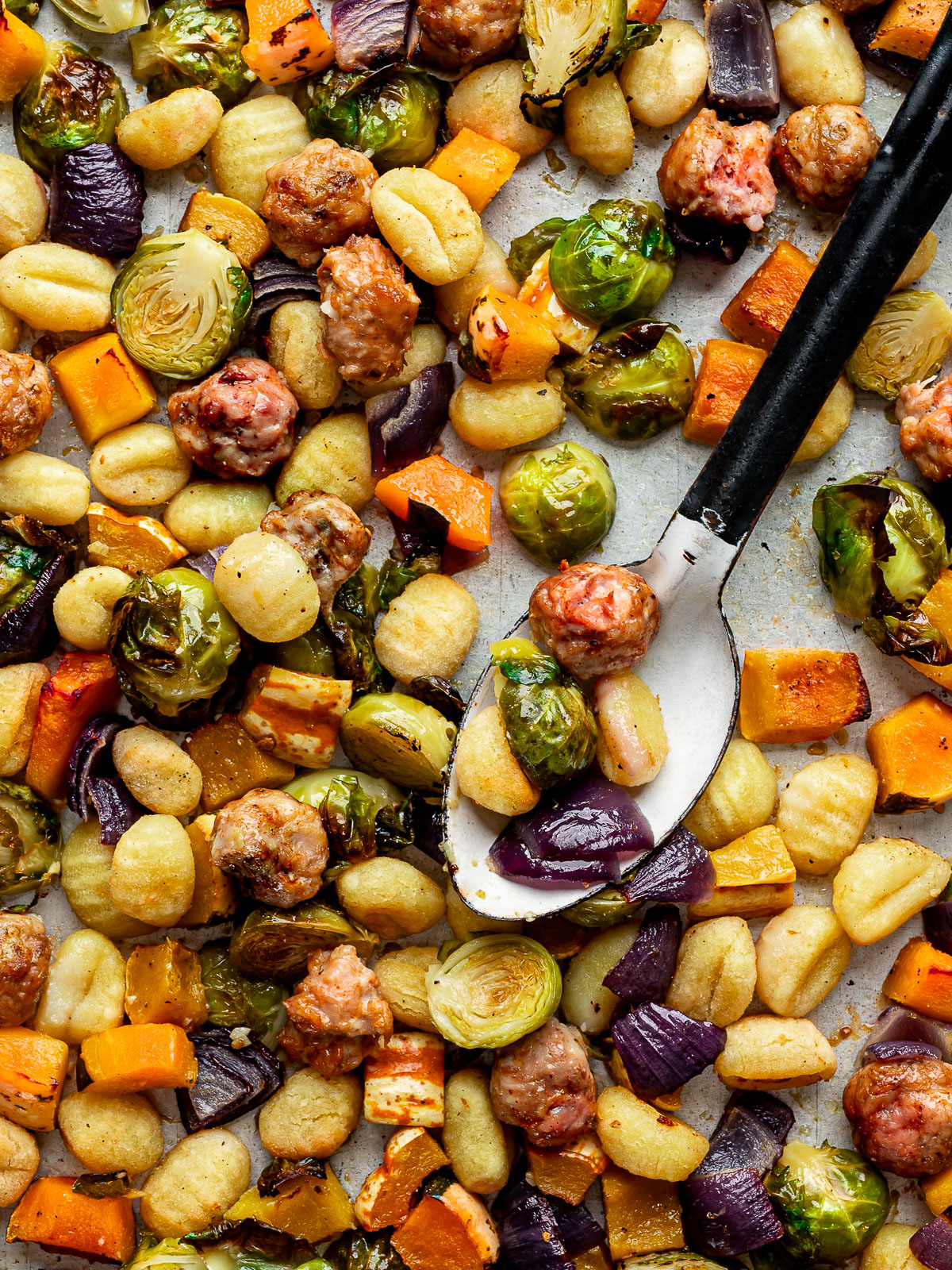 Baked gnocchi with Brussels sprouts, squash, sausage and red onion on a sheet pan.