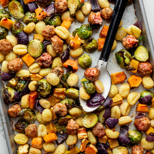 Baked gnocchi with Brussels sprouts, squash, sausage and red onion on a sheet pan.