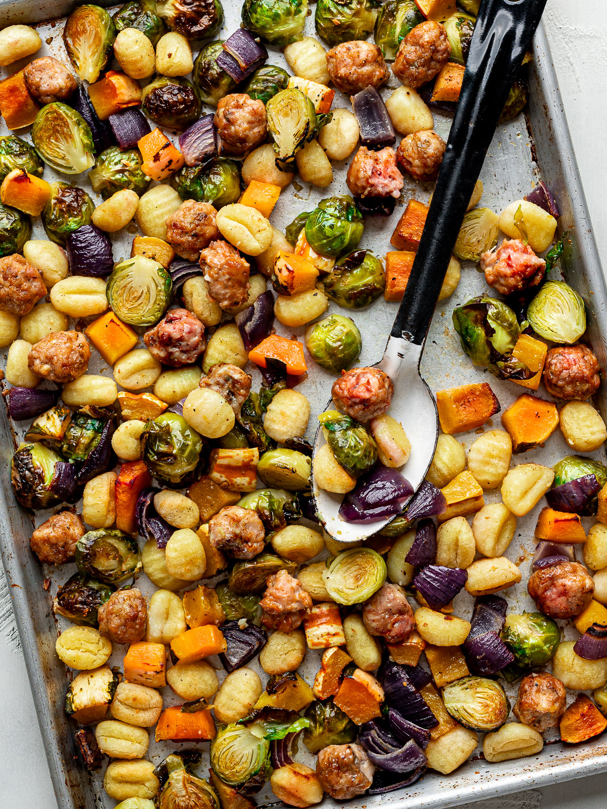 Baked gnocchi with Brussels sprouts, squash, sausage and red onion on a sheet pan.